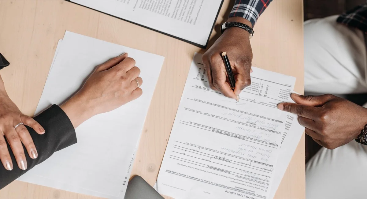 Two people completing printed forms and paperwork at a desk